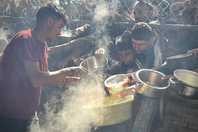 25 de maio de 2025, Khan Younis, Faixa de Gaza, Território Palestino: Os palestinos esperam em longas filas para receber potes de comida distribuídos por organizações de caridade, enquanto enfrentam uma crise alimentar, na área de Al-Mawasi em Khan Yunis,