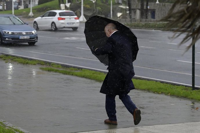 Archivo - Un hombre con paraguas trata de refugiarse del viento y de la lluvia