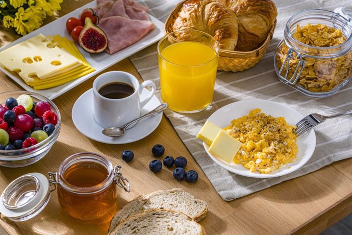 Archivo - Desayuno saludable a base de huevos revueltos, queso, jamón, café, croissants y zumo de frutas