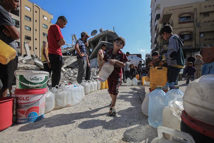 03 de junho de 2025, Territórios Palestinos, Gaza: Crianças palestinas carregam galões cheios de água distribuídos por um caminhão-tanque. Os palestinos estão enfrentando dificuldades para ter acesso à água devido aos contínuos ataques israelenses à Faixa