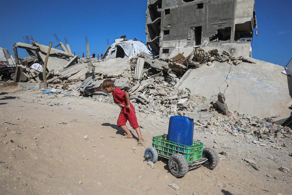 Niño palestino traslada bidones llenos de agua distribuidos por un camión cisterna en Gaza