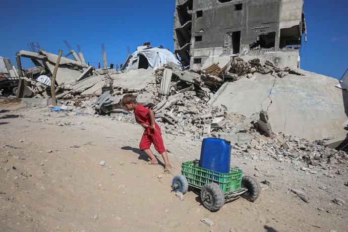 03 de junho de 2025, Territórios Palestinos, Gaza: Uma criança palestina puxa galões cheios de água distribuídos por um caminhão-tanque. Os palestinos estão enfrentando dificuldades para ter acesso à água devido aos contínuos ataques israelenses à Faixa d