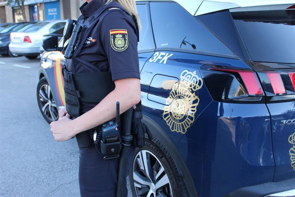 Archivo - Imagen de una agente y de un coche patrulla de la Policía Nacional.