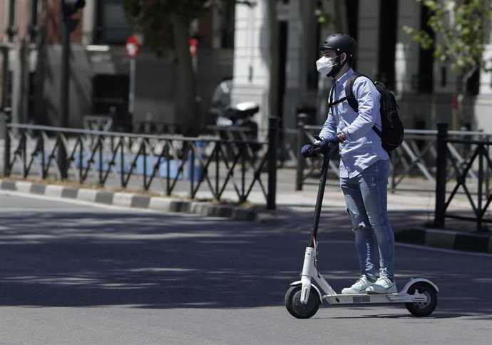 Archivo - Un hombre protegido con mascarilla monta en un patinete eléctrico.