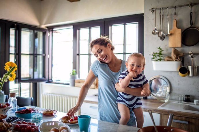 Archivo - Multitarea de una madre cuidando a su bebé, cocinando y hablando por teléfono.