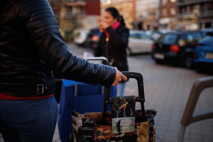 Archivo - Una mujer con un carro de la compra en una fila para recibir alimentos.