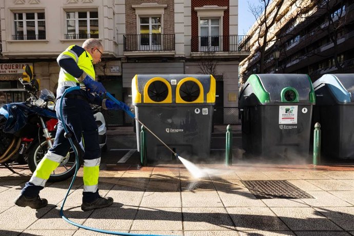 Un operario limpia una acera con agua a presión.