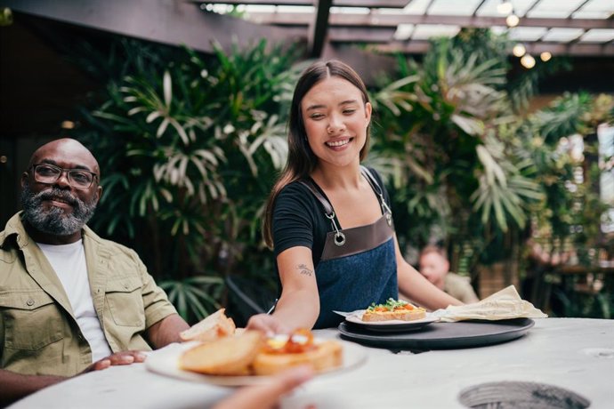 Archivo - Smiling young waitress, bringing the order in a restaurant, serving a family during their vacations
