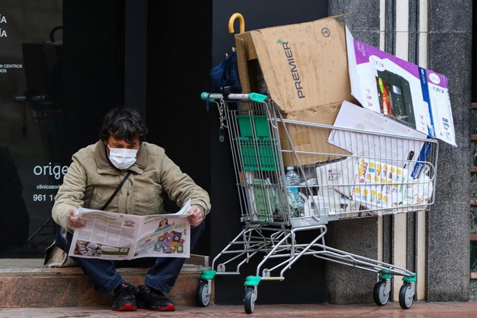 Archivo - Una persona sin hogar lee un periódico junto a un carrito lleno de cartones durante el estado de alarma decretado por el coronavirus en las proximidades del Hospital La Fe, en Valencia (Comunidad Valenciana) a 27 de marzo de 2020.