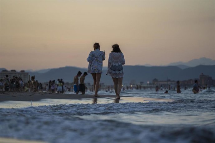 Archivo - Dos personas pasean por la playa de la Malvarrosa durante un atardecer