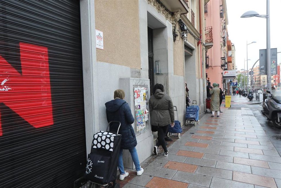 Archivo - Un fila de personas espera a entrar en economato solidario de Cáritas durante la pandemia.