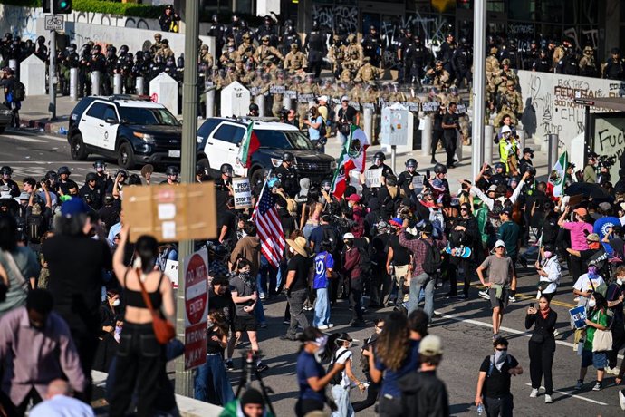 09 June 2025, US, Los Angeles: People protest in downtown Los Angeles while National Guard troops stand in front of a government building. Demonstrators gather to protest against the US government's migration policy. The Pentagon announces the deployment 