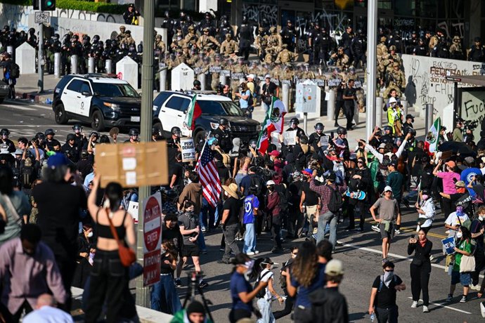 09 de junho de 2025, EUA, Los Angeles: Pessoas protestam no centro de Los Angeles enquanto tropas da Guarda Nacional ficam em frente a um prédio do governo. Os manifestantes se reúnem para protestar contra a política de migração do governo dos EUA. O Pent
