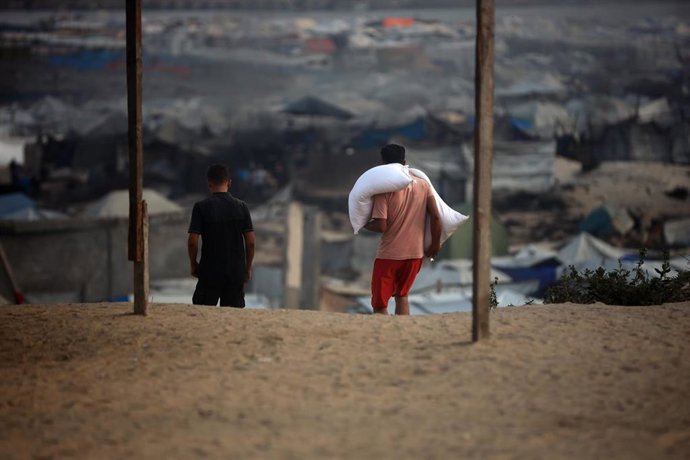 Dos gazatíes desplazados caminan a lo lejos mientras una porta un saco de harina