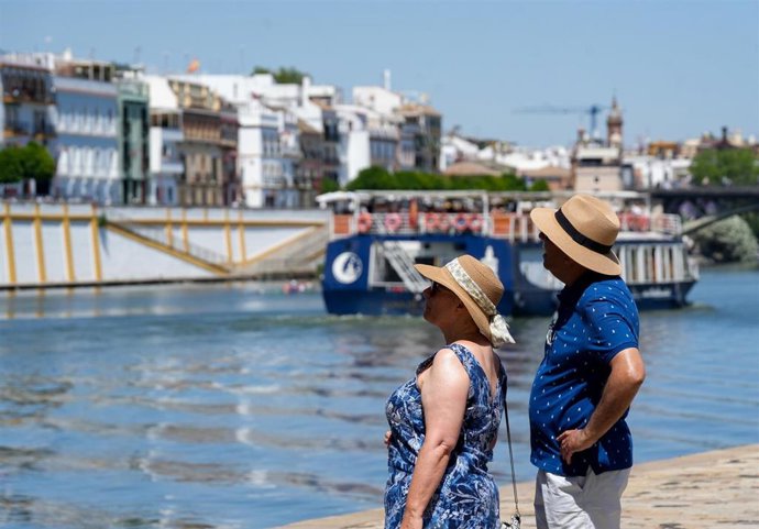 Personas con ropa veraniega paseando junto al río en Sevilla. 