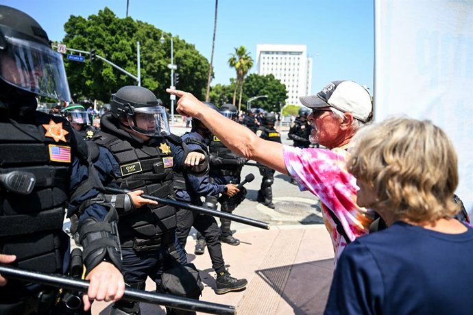 09 de junho de 2025, EUA, Los Angeles: Um homem fica em frente a funcionários durante protestos no centro de Los Angeles. Manifestantes se reúnem para protestar contra a política de migração do governo dos EUA. O Pentágono anuncia o envio de mais 2.000 so