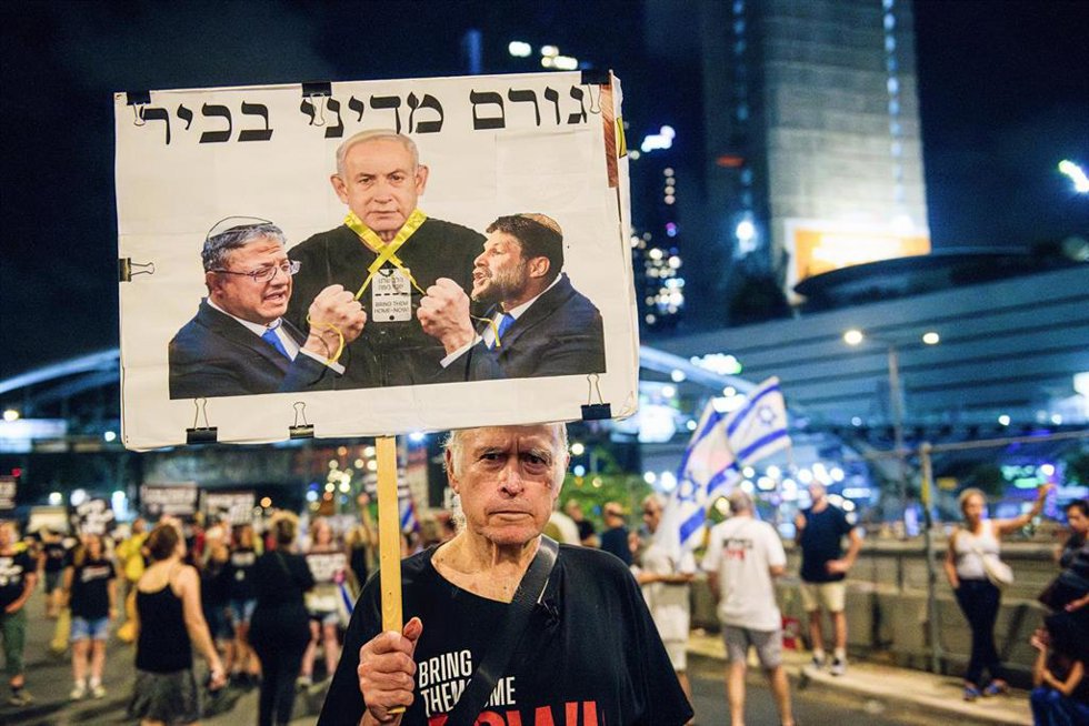 Archivo - Un manifestante sostiene una pancarta con los rostros del ministro de Finanzas y el de Seguridad de Israel asfixiando al primer ministro
