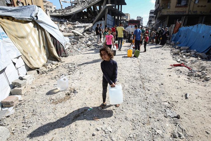 03 de junho de 2025, Territórios Palestinos, Gaza: Uma criança palestina carrega galões cheios de água distribuídos por um caminhão-tanque. Os palestinos estão enfrentando dificuldades para ter acesso à água devido aos contínuos ataques israelenses à Faix