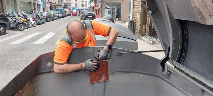 Operario de Emulsa (Gijón) coloca una placa antiolor en un contenedor.