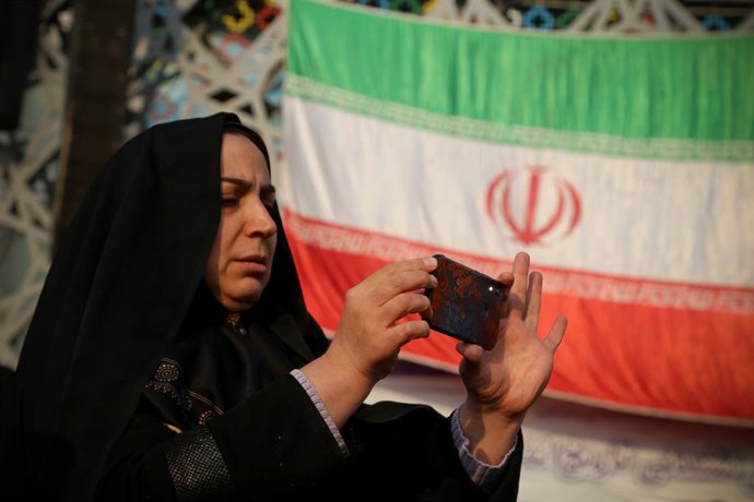 Archivo - 29 de dezembro de 2022, Teerã, Teerã, Irã: Uma mulher velada tira uma foto com seu telefone celular enquanto está em frente à bandeira iraniana durante a manifestação do aniversário de 9 de dezembro na Praça Imam Hossein, no centro de Teerã, Irã
