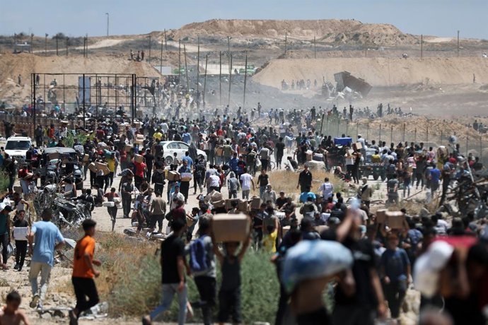 Palestinos carregam ajuda entregue pela GHF, apoiada por Israel e pelos EUA, em Al Bureij, na região central da Faixa de Gaza.