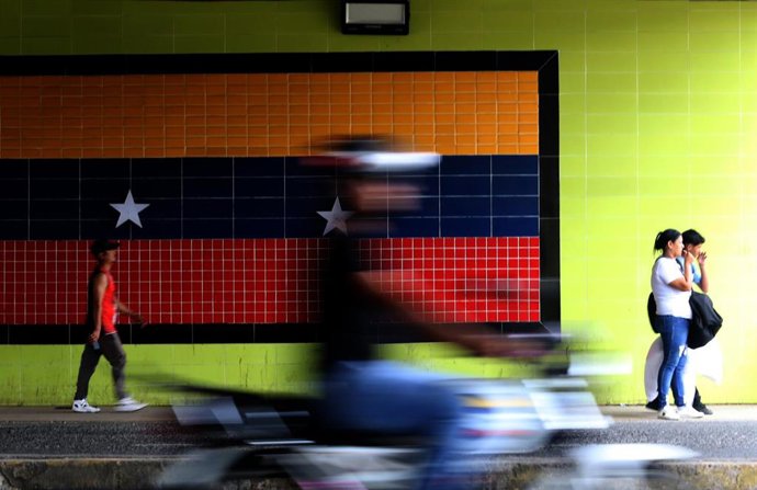 Archivo - Un grupo de personas pasa ante un mural con la bandera en la ciudad venezolana de Valencia