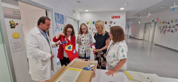 La delegada territorial de Salud y Consumo en Cádiz, Eva Pajares, e director gerente del Área de Gestión Sanitaria Campo de Gibraltar Este, Sergio Calderón, y la responsable de Fundación Moeve en Cádiz, Estrella Blanco, miran los kits de superhéroes