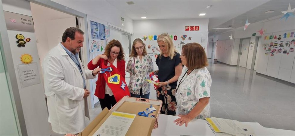 La delegada territorial de Salud y Consumo en Cádiz, Eva Pajares, e director gerente del Área de Gestión Sanitaria Campo de Gibraltar Este, Sergio Calderón, y la responsable de Fundación Moeve en Cádiz, Estrella Blanco, miran los kits de superhéroes