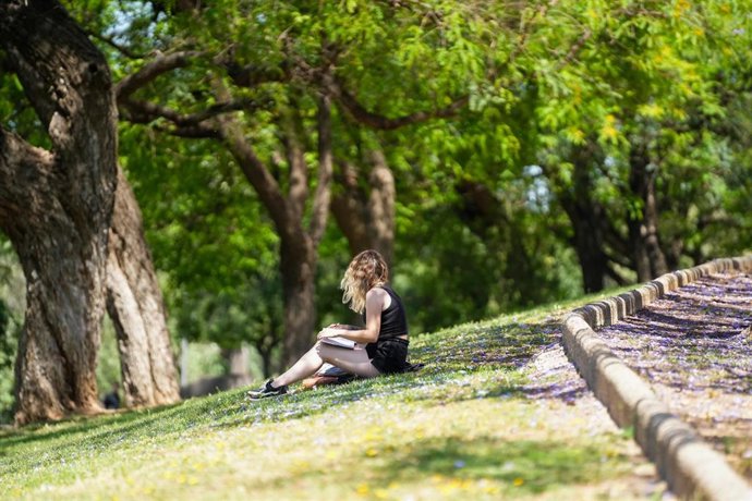 Una mujer con ropa veraniega leyendo junto al río, en una imagen de archivo.