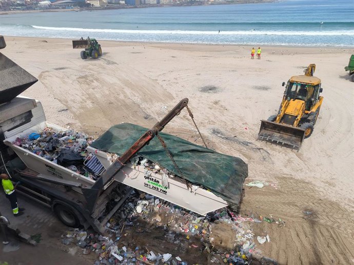 Los servicios de limpieza despejan de basura y residuos la playa de Riazor tras las hogueras de la noche de San Juan, en A Coruña