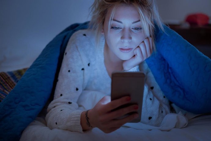 Archivo - Mujer mirando el móvil por la noche en la cama.