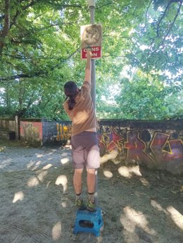 Un padre limpia el cartel que indica que no están permitidos los perros en el parque infantil de A Trisca, en Santiago