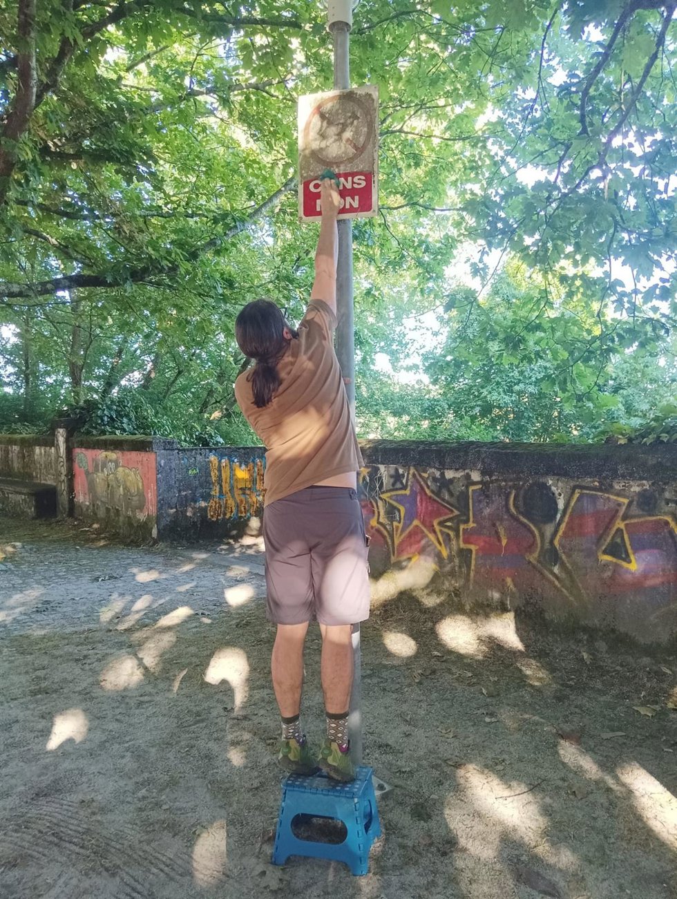 Un padre limpia el cartel que indica que no están permitidos los perros en el parque infantil de A Trisca, en Santiago