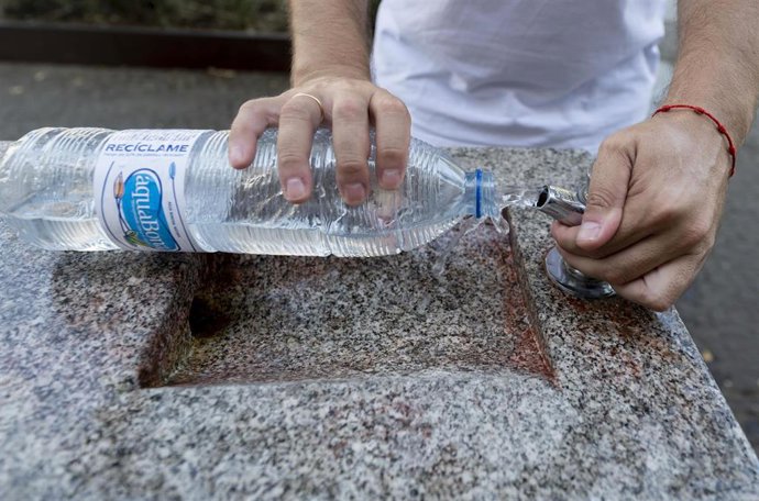 Archivo - Una persona llena una botella de agua de una fuente.