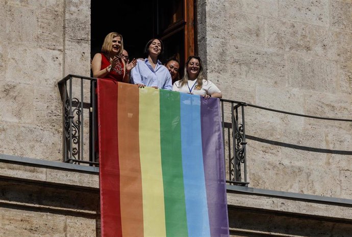 La delegada del Gobierno en la Comunitat, Pilar Bernabé (i), y la secretaria general del PSPV-PSOE y ministra de Ciencia, Innovación y Universidades, Diana Morant (c), despliegan la bandera LGTBI en la fachada de Delegación del Gobierno en la Comunitat.