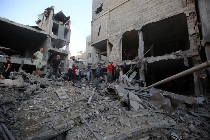 Un grupo de palestinos entre los escombros de un edificio destruido en la ciudad de Gaza