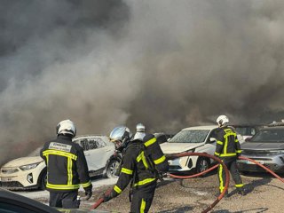 Efectivos de los bomberos tratan de sofocar un incendio que afecta a un aparcamiento con más de 100 vehículos aparcados