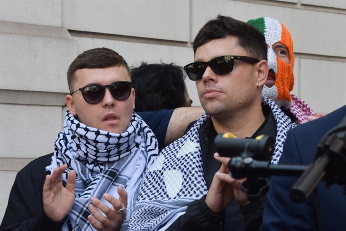18 de junho de 2025, Londres, Reino Unido: Os membros do Kneecap, Mo Chara (à esquerda), Moglai Bap (à direita) e DJ Provai (atrás), batem palmas durante um discurso do lado de fora do Tribunal de Magistrados de Westminster. Mo Chara, membro do grupo de r