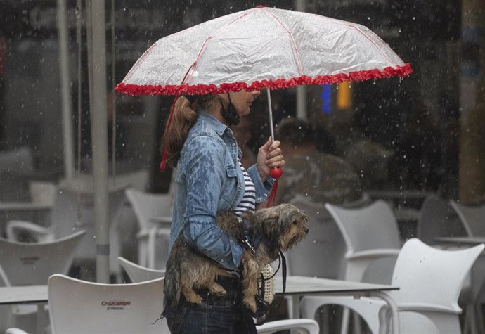 Archivo - Una mujer lleva a su perro en brazos bajo una tormenta, en una imagen de archivo.