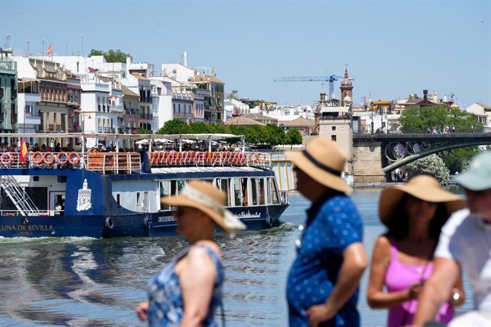 Archivo - Personas con ropa veraniega paseando junto al río Guadalquivir en Sevilla, en una imagen de archivo. 