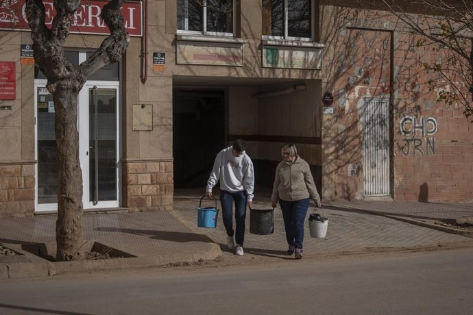 Archivo - Dos personas con cubos salen de un garaje del barrio de la Fuente, a un mes del paso de la DANA por Valencia, a 29 de noviembre de 2024, en Utiel, Valencia
