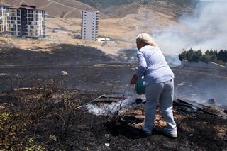 July 2, 2025, Izmir, Turkey: A woman pours water with a bucket to put out the fire. In Izmir, the western city of Turkey, forest fires have been out of control for days as temperatures and winds rise. Thousands of hectares of land were burned in various p