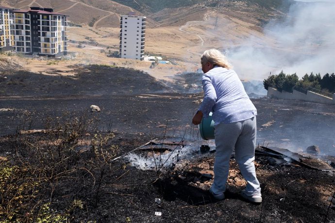 2 de julho de 2025, Izmir, Turquia: Uma mulher despeja água com um balde para apagar o fogo. Em Izmir, a cidade ocidental da Turquia, os incêndios florestais estão fora de controle há dias devido ao aumento das temperaturas e dos ventos. Milhares de hecta