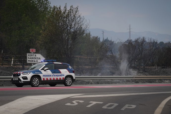 Un vehículo de los Mossos d'Esquadra junto a humo del incendio de Paüls en la carretera de Aldover