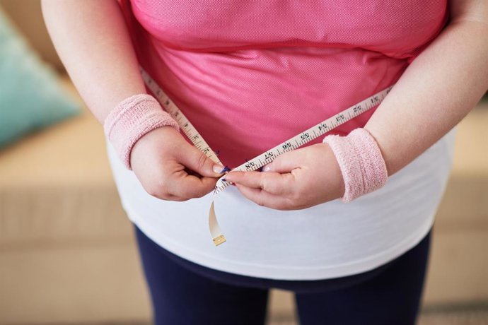 Archivo - Close-up of overweight woman measuring her waist with tape measure
