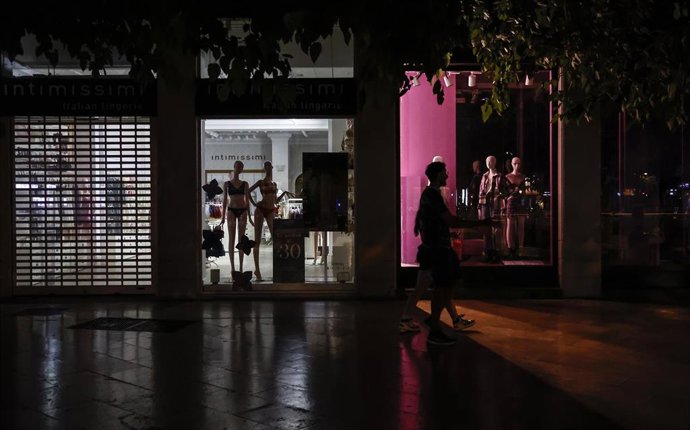 Archivo - Varias personas caminan al lado de escaparates apagados