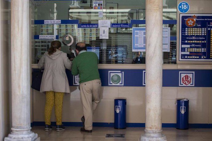 Archivo - Dos personas compran lotería en una Administración. Imagen de archivo. 