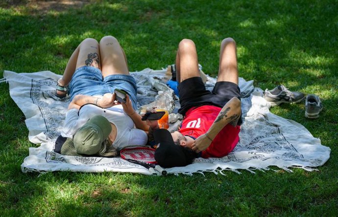 Archivo - Personas con ropa veraniega descansan junto al río. Imagen de archivo. 