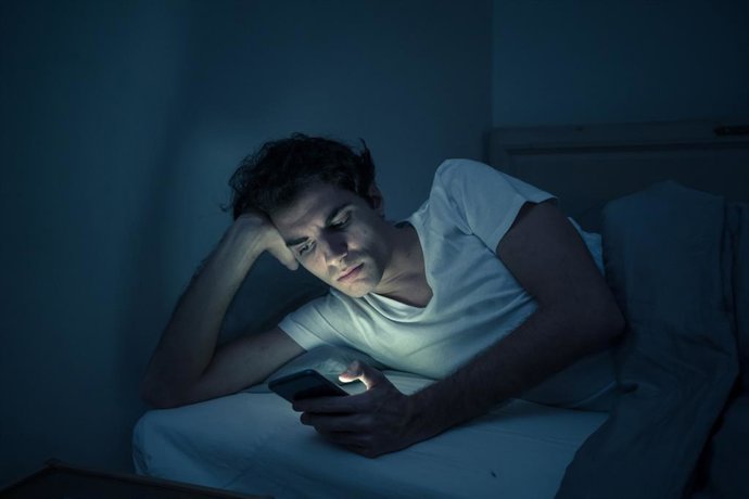 Archivo - Hombre con insomnio mirando el móvil en la cama.