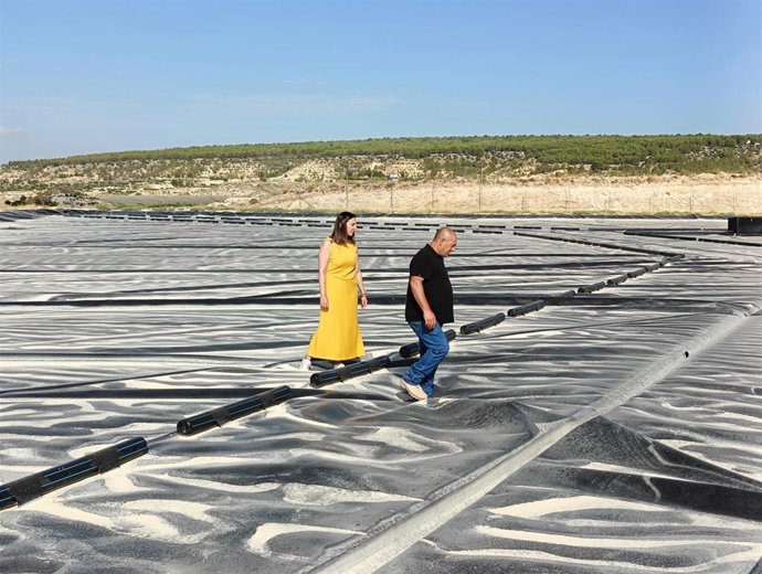 Imagen de la consejera junto a uno de los beneficiarios de las ayudas con las que ha cubierto el embales de agua sobre el que caminan.
